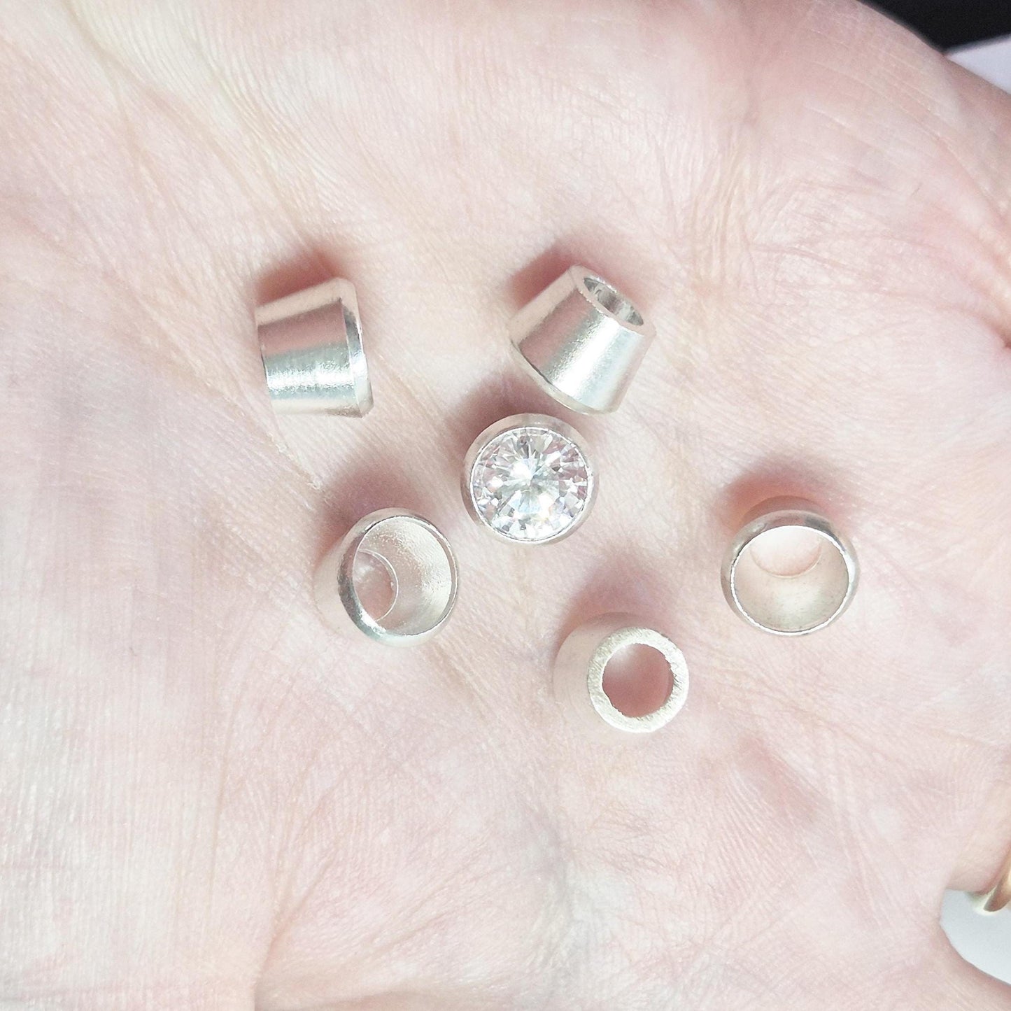 Sterling silver bezel cups and round gemstone shown in hand for scale, tapered bezel settings for jewellery making.
