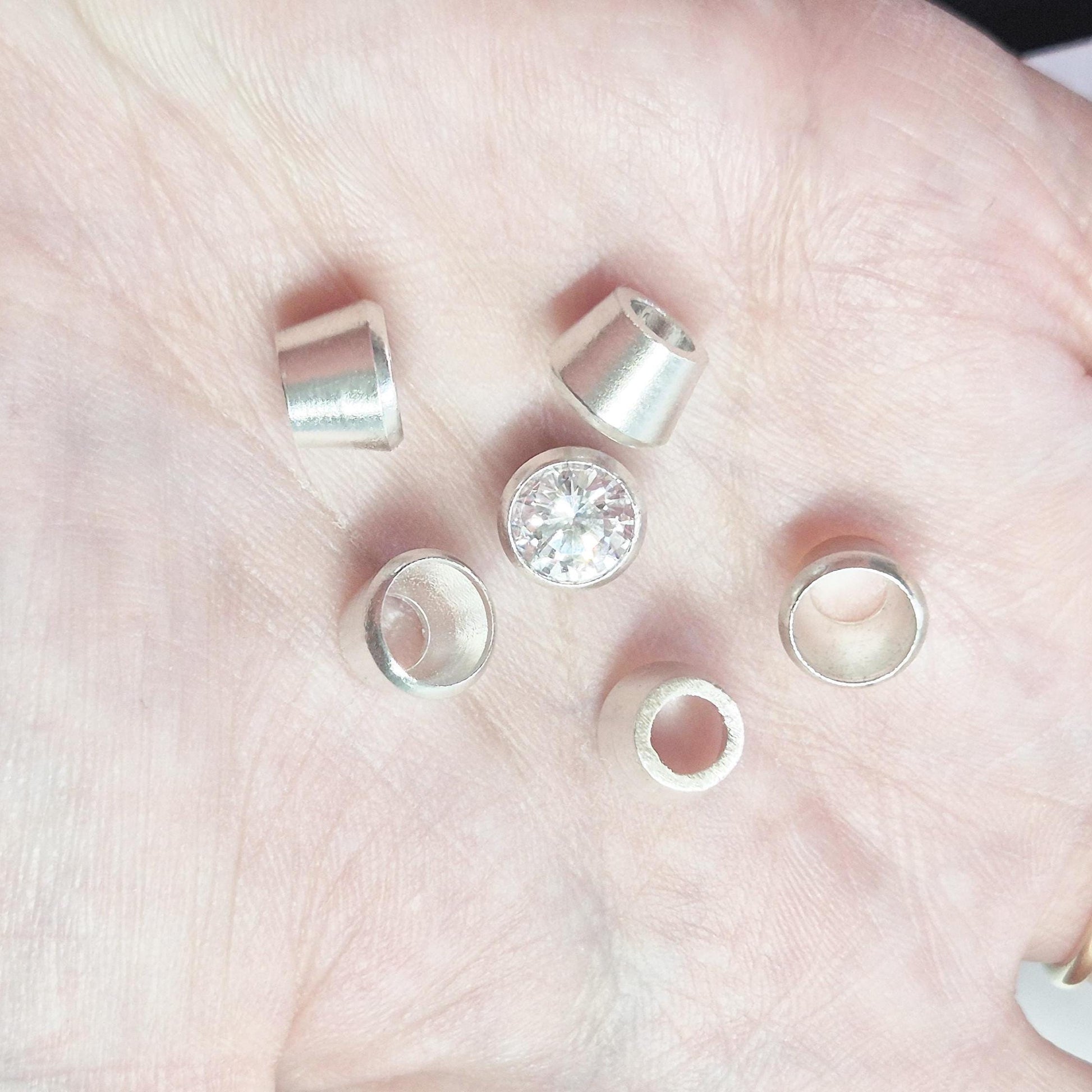 Sterling silver bezel cups and round gemstone shown in hand for scale, tapered bezel settings for jewellery making.