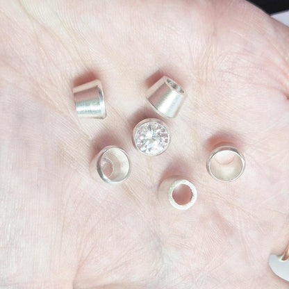 Sterling silver bezel cups and round gemstone shown in hand for scale, tapered bezel settings for jewellery making.