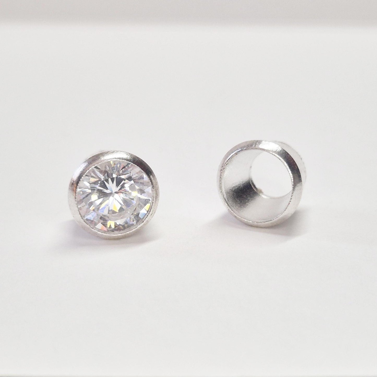 Finished round gemstone set in sterling silver bezel beside empty bezel cup, jewellery setting component on white background.
