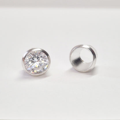 Finished round gemstone set in sterling silver bezel beside empty bezel cup, jewellery setting component on white background.