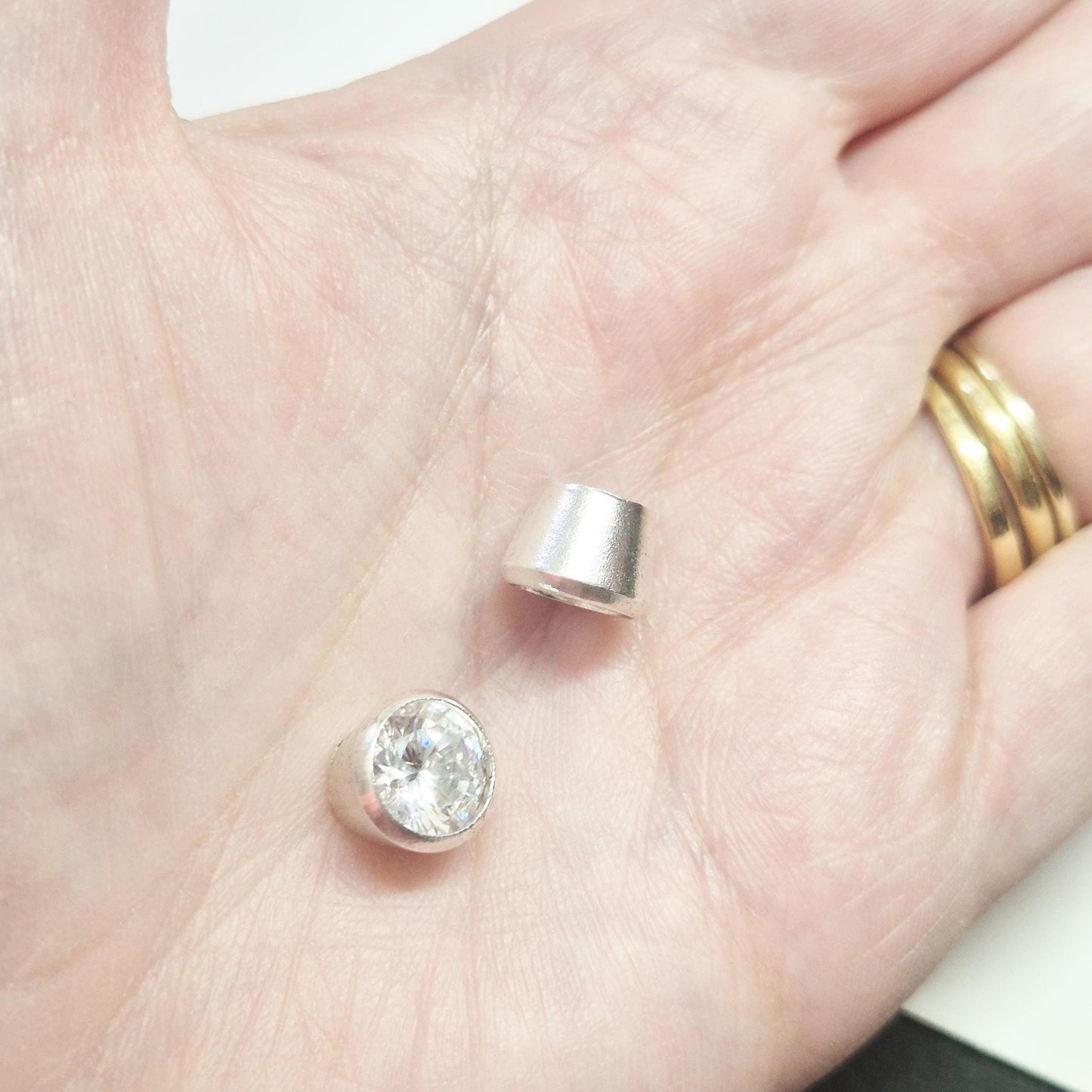 Sterling silver bezel cups and round gemstone shown in hand for scale, tapered bezel settings for jewellery making.