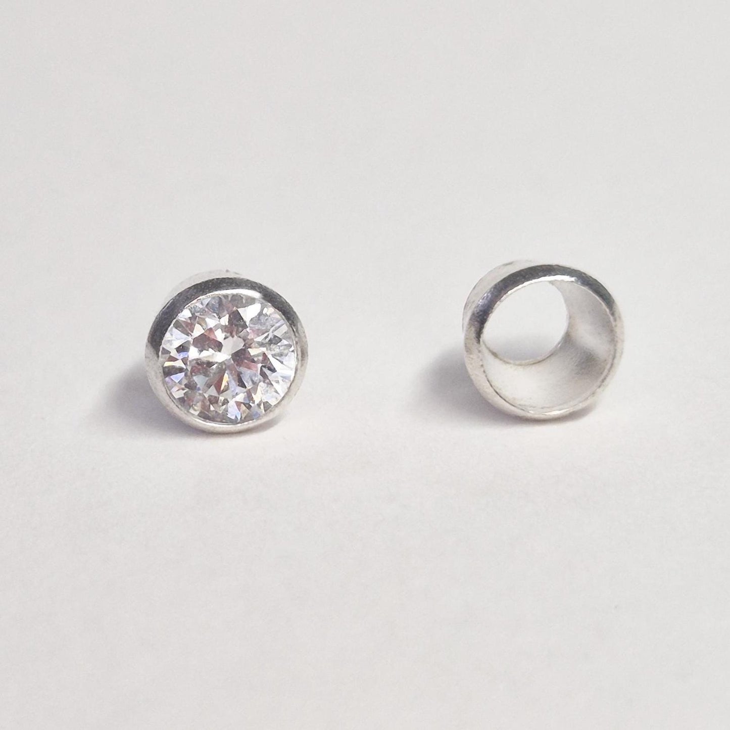 Finished example of round gemstone set in sterling silver bezel next to empty bezel cup, demonstrating jewellery setting component.