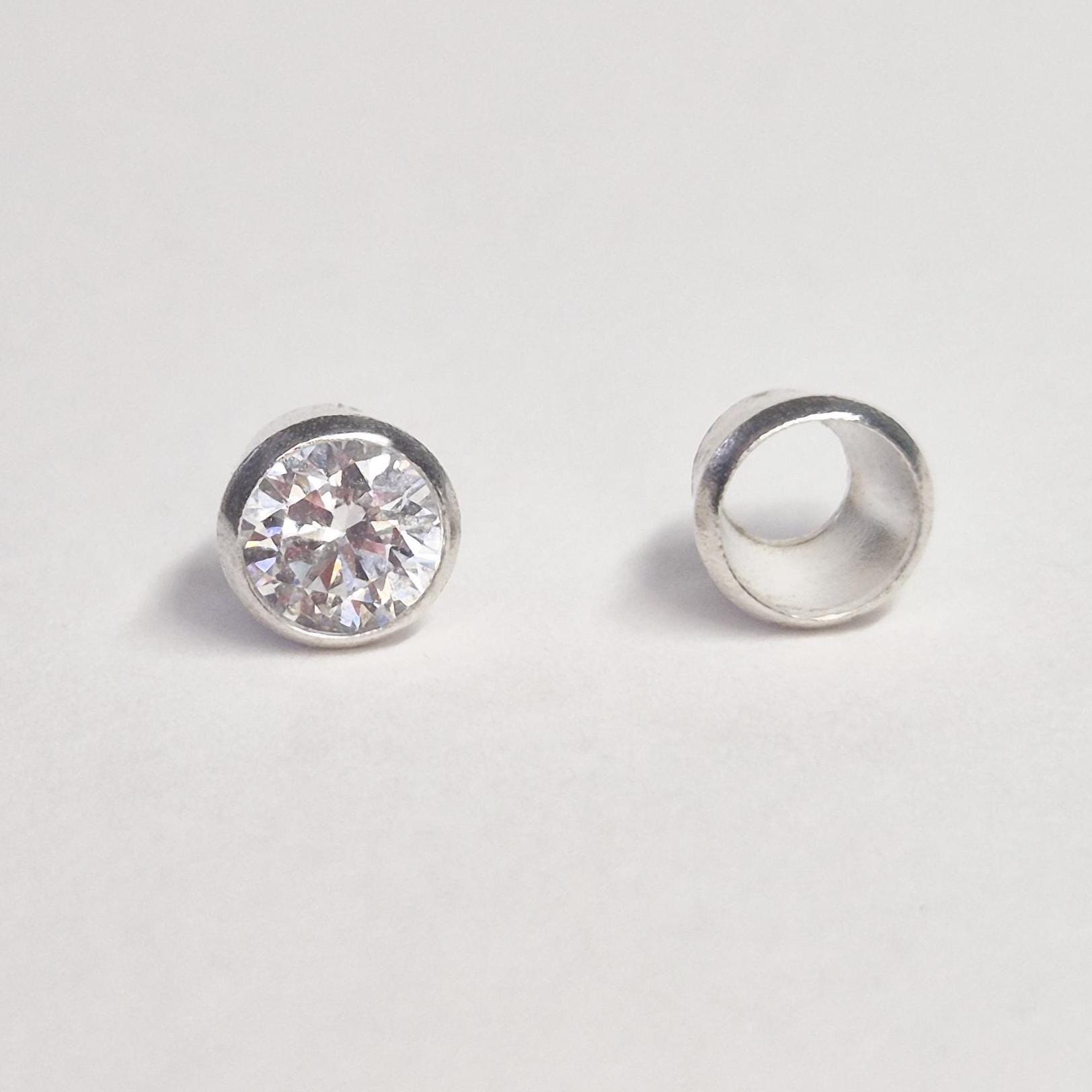 Finished example of round gemstone set in sterling silver bezel next to empty bezel cup, demonstrating jewellery setting component.