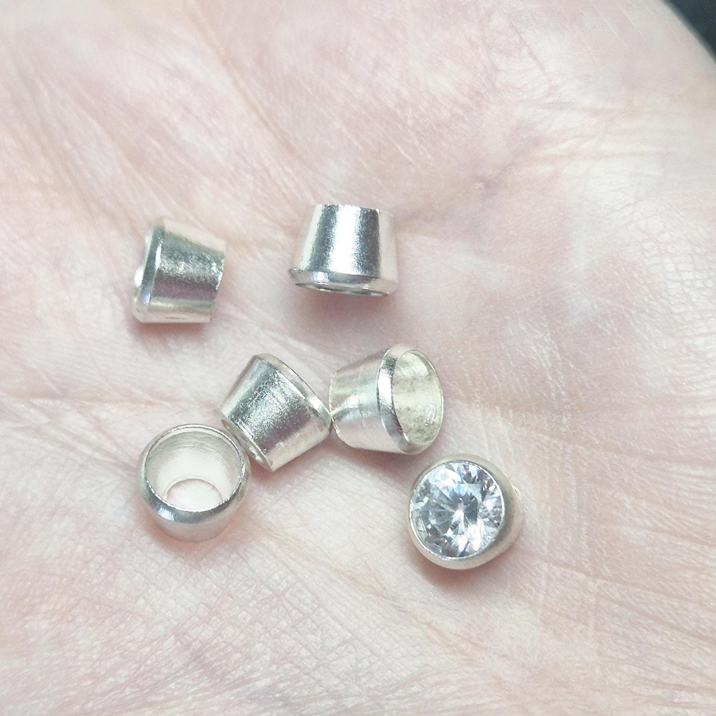 Sterling silver bezel cups and round gemstone shown in hand for scale, tapered bezel settings for jewellery making.