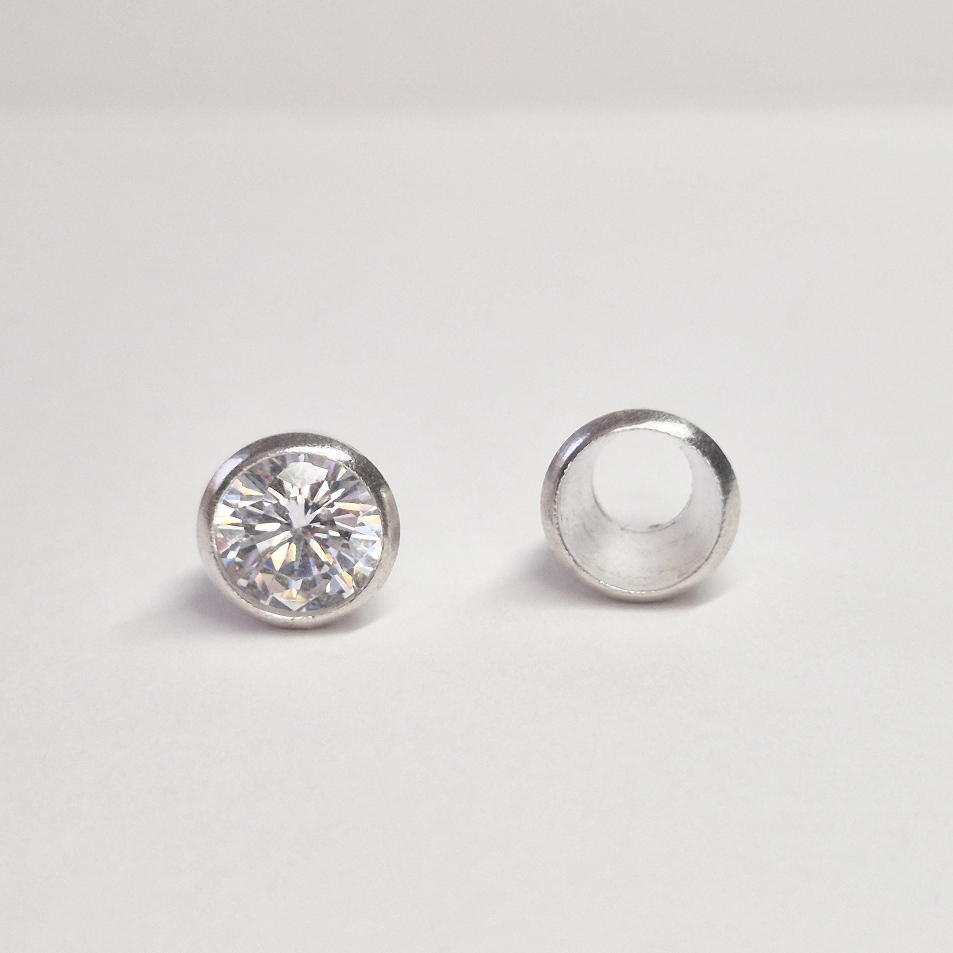 Finished round gemstone set in sterling silver bezel beside empty bezel cup, jewellery setting component on white background.