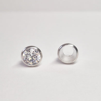 Finished round gemstone set in sterling silver bezel beside empty bezel cup, jewellery setting component on white background.