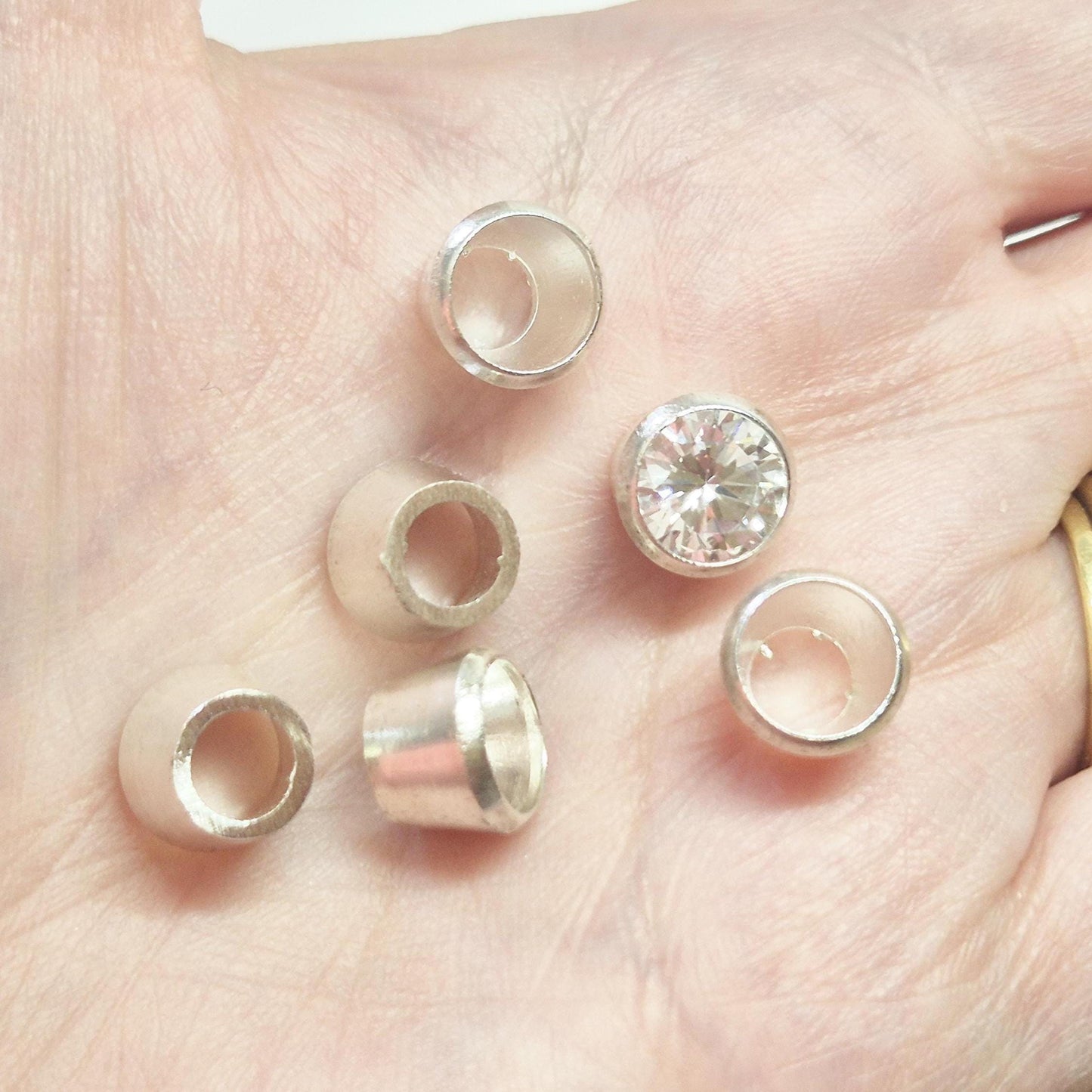 Sterling silver bezel cups and round gemstone shown in hand for scale, tapered bezel settings for jewellery making.