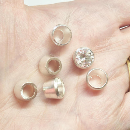 Sterling silver bezel cups and round gemstone shown in hand for scale, tapered bezel settings for jewellery making.