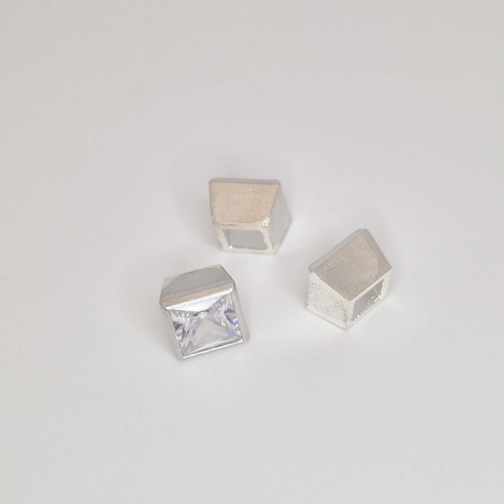 Close-up of square princess cut stone partially set in a sterling silver bezel with additional setting components nearby.