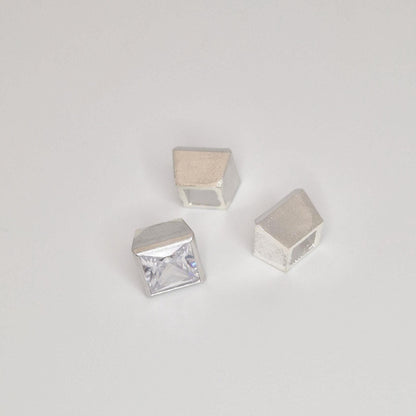 Close-up of square princess cut stone partially set in a sterling silver bezel with additional setting components nearby.
