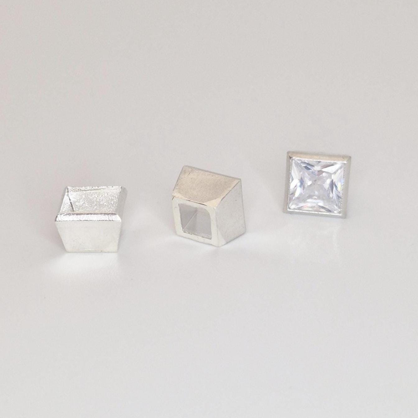 Sterling silver square bezel setting components and princess cut gemstone arranged for product display.