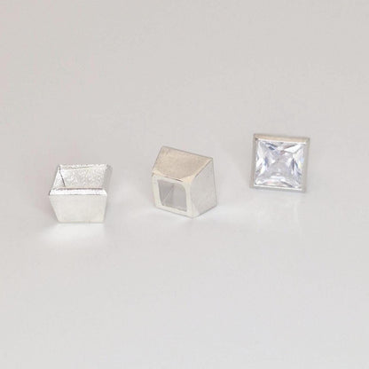 Sterling silver square bezel setting components and princess cut gemstone arranged for product display.