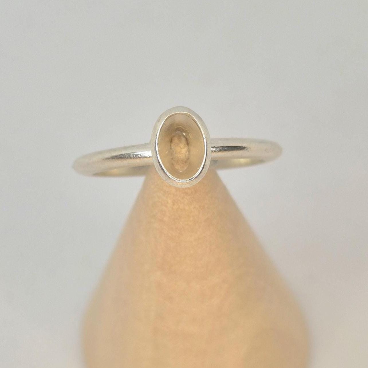 An argentium silver 6x4mm Oval Bezel Ring on a wooden display cone.