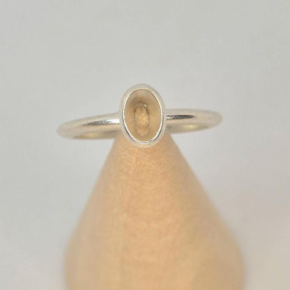 An argentium silver 6x4mm Oval Bezel Ring on a wooden display cone.
