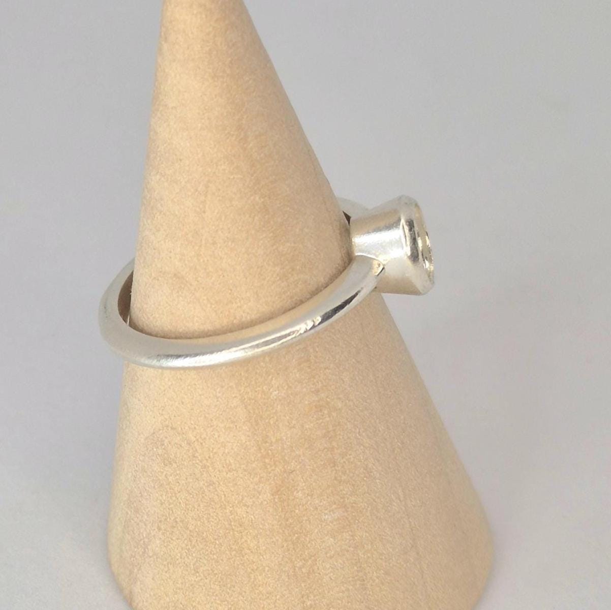 Side view of a silver 6x4mm Oval Bezel Ring on a wooden display cone.