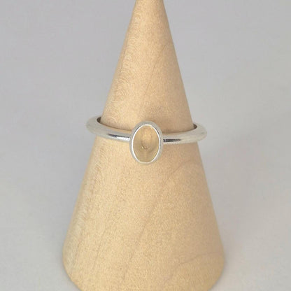 Front view of a sterling or argentium silver 6x4mm Oval Bezel Ring on the middle of a wooden display cone against a white background.