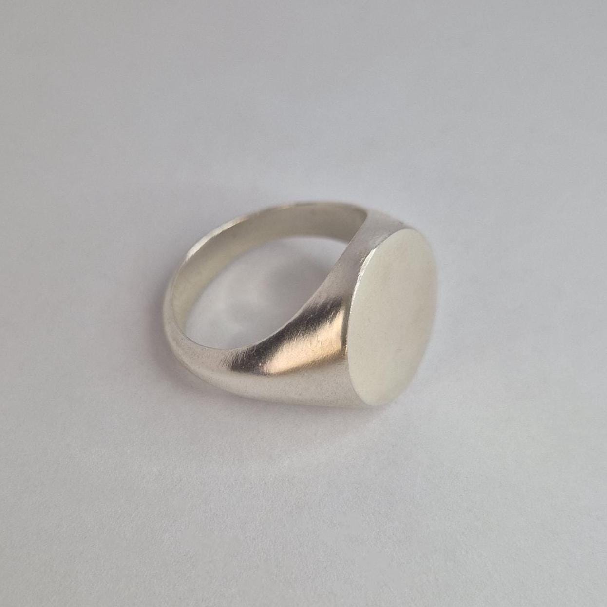 Angled view of heavy round signet ring, polished sides with flat engraving face