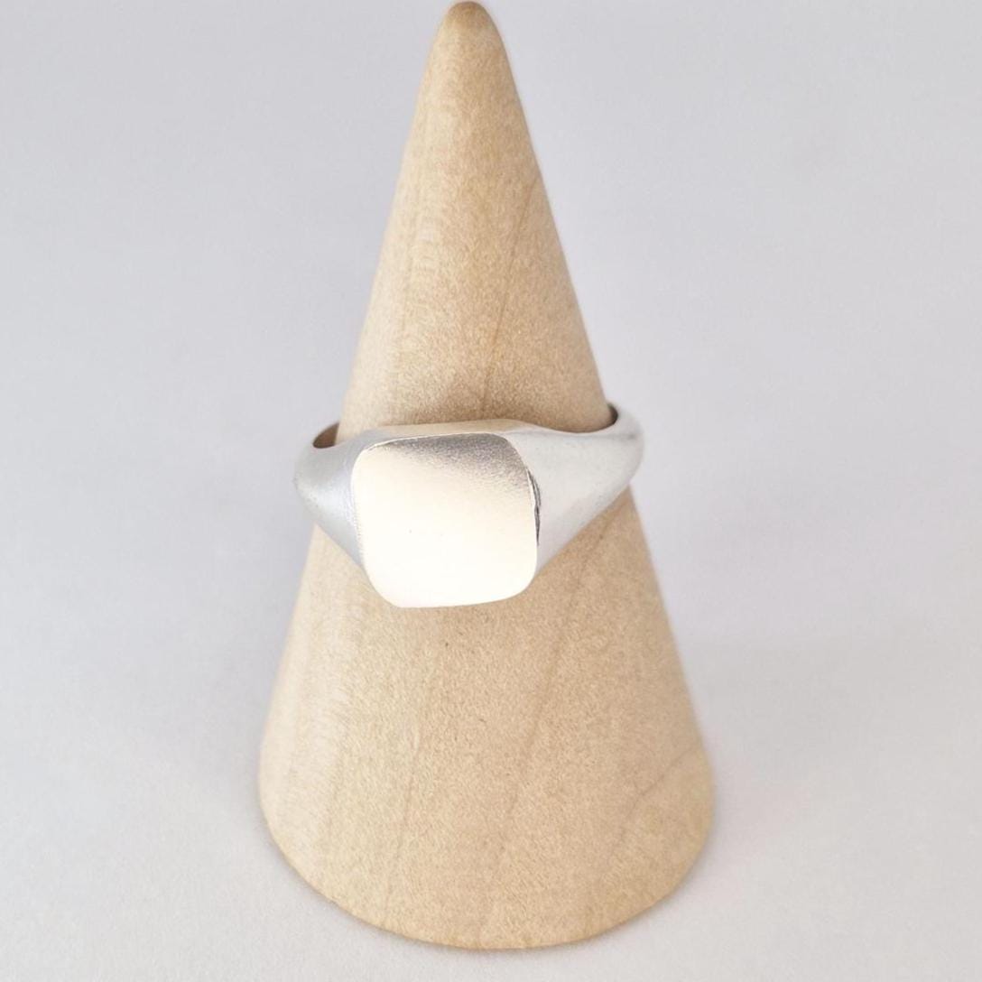 Front view of square cushion signet ring in sterling silver on wooden stand, matte face detail