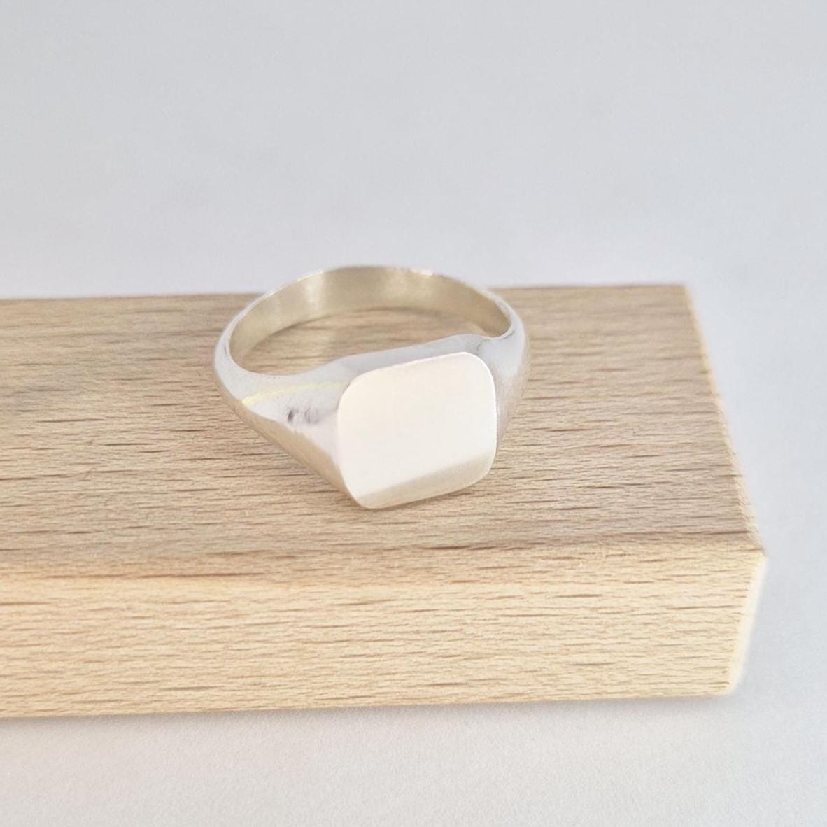 Angled view of cushion signet ring in sterling silver on wooden block, clean modern design