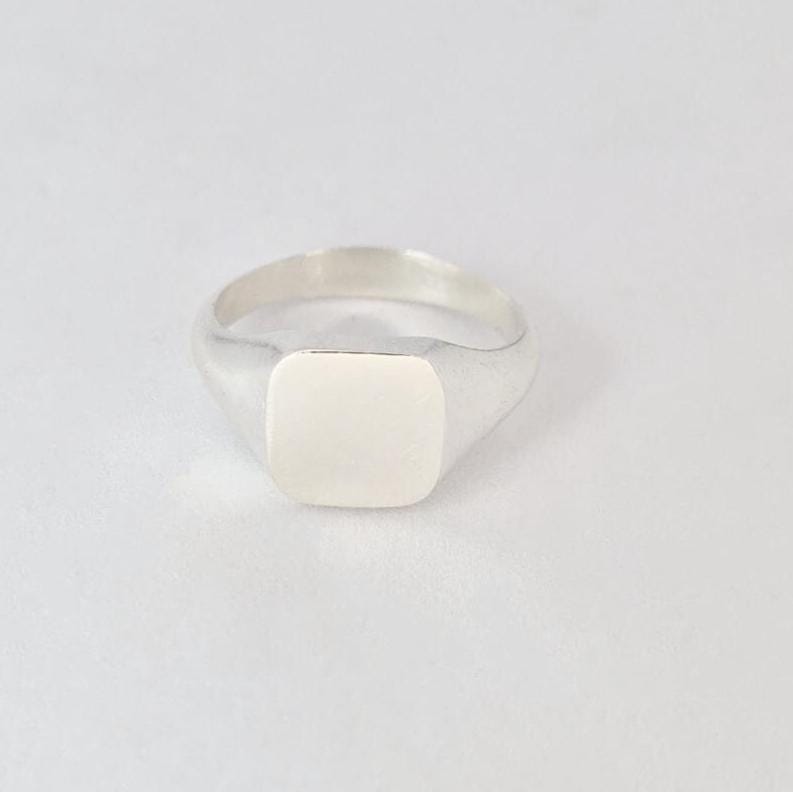 Close-up of cushion signet ring face in silver with soft brushed texture and rounded edges