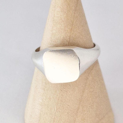 Close-up of cushion signet ring face in silver with soft brushed texture and rounded edges