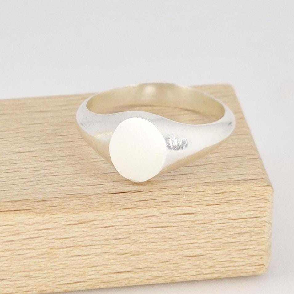 Polished oval signet ring in sterling or Argentium silver on wooden block, angled front view highlighting smooth face