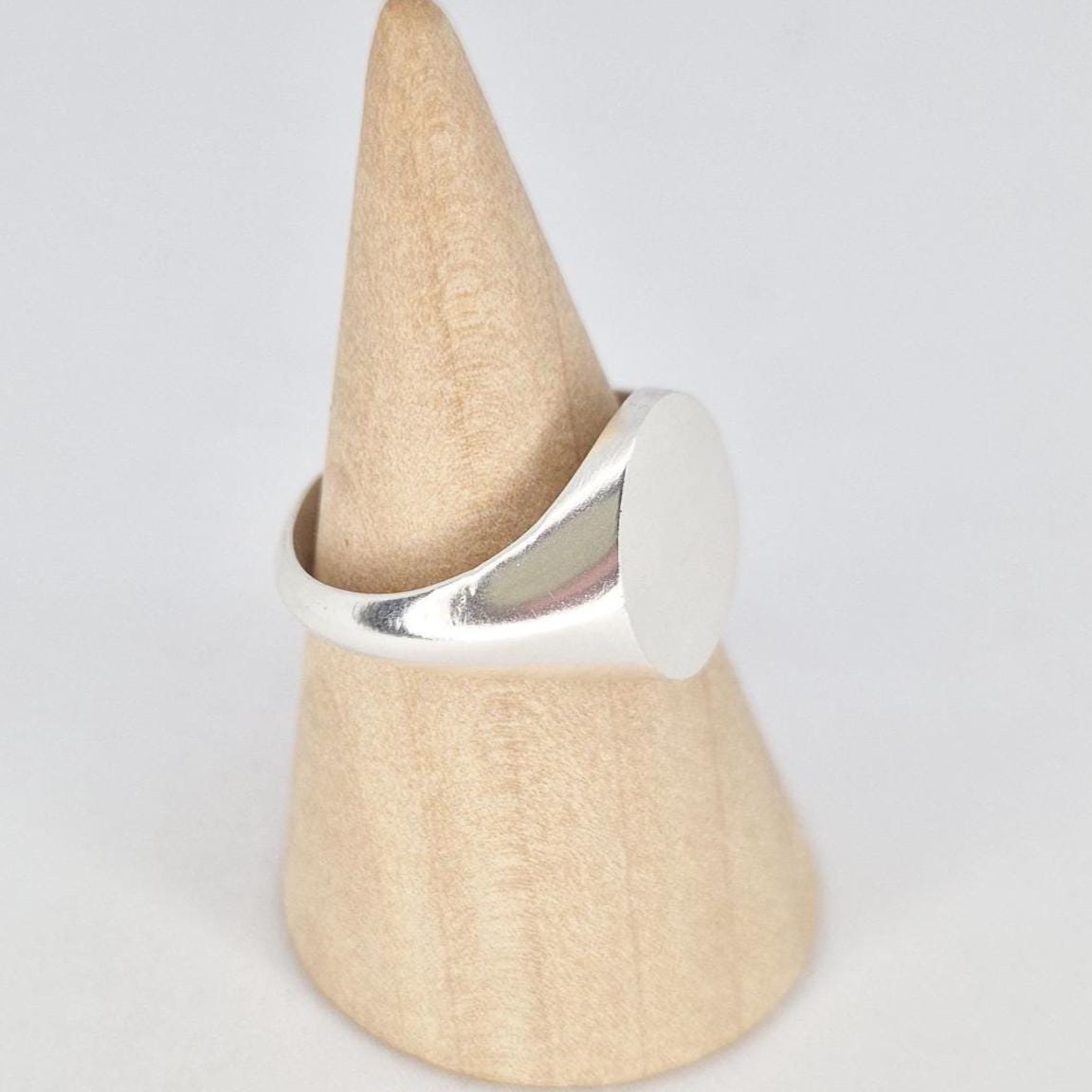 Side view of oval silver signet ring on wooden cone stand highlighting tapered shoulders