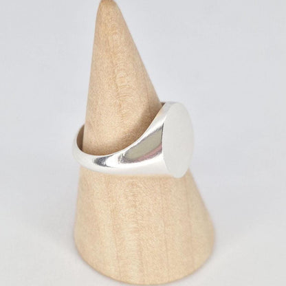 Side view of oval silver signet ring on wooden cone stand highlighting tapered shoulders