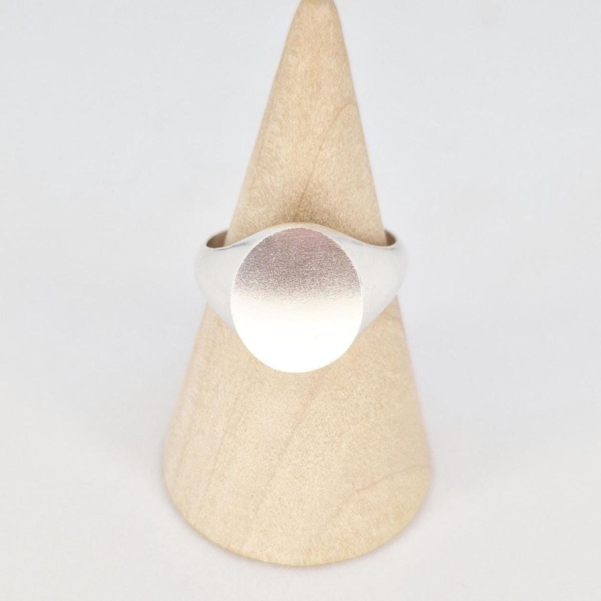 Front view of oval signet ring on wooden stand showing satin-finished oval face