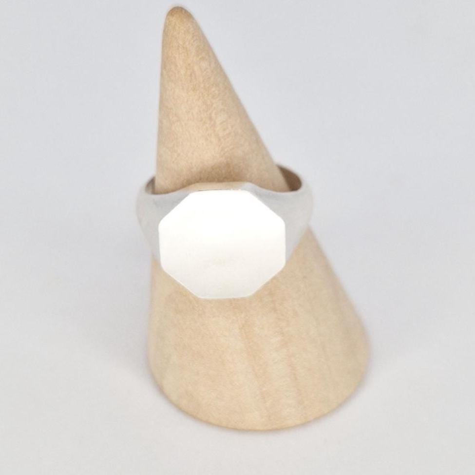 Octagon signet ring displayed on wooden stand showing clean geometric face and soft satin texture