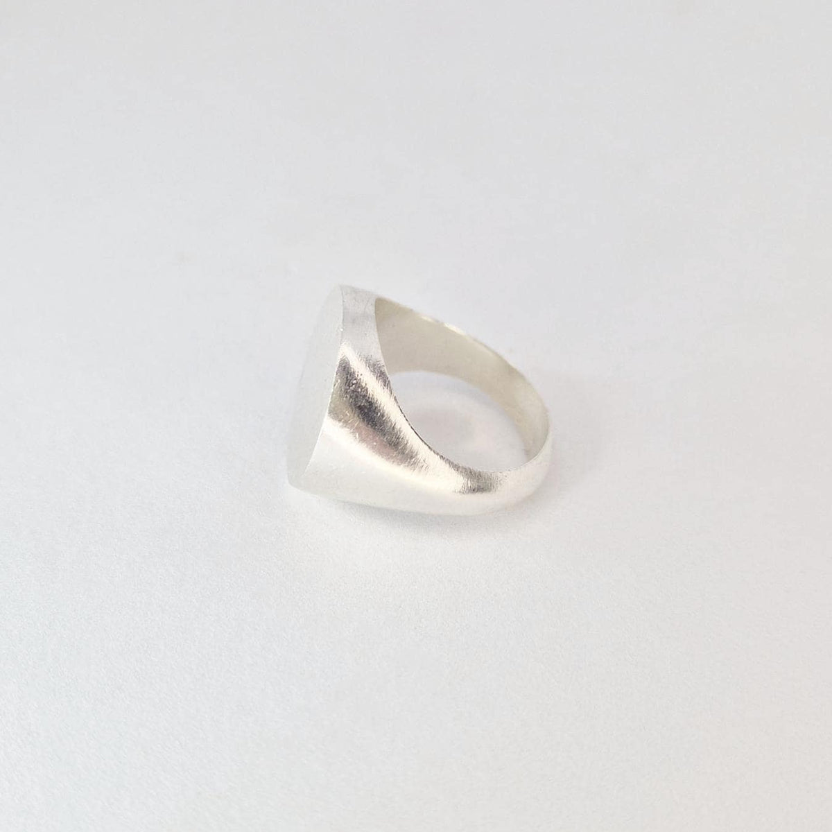 Side profile of heavy round signet ring displaying thick band and gradual taper into flat circular face.