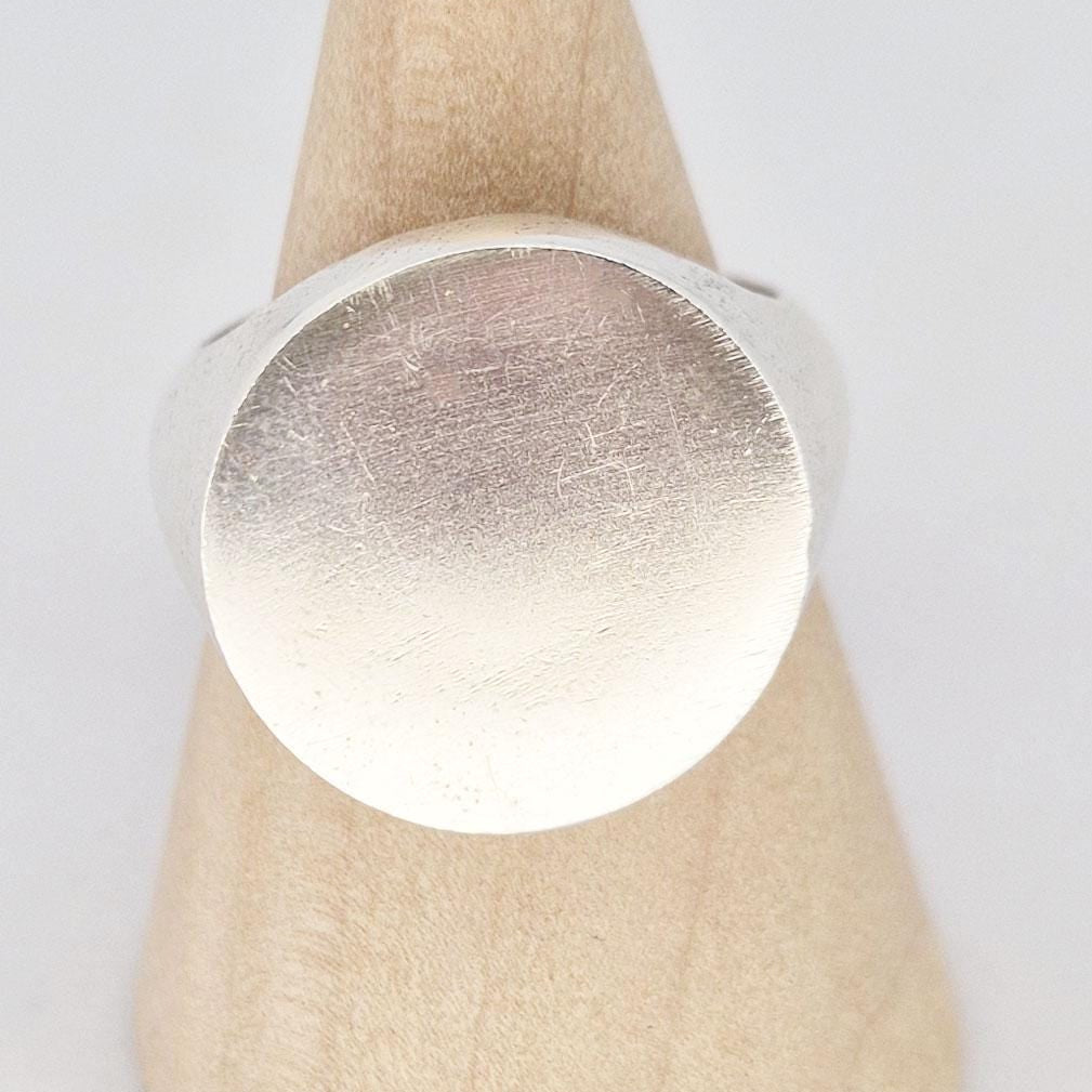 Macro close-up of round signet ring face showing brushed satin texture and subtle surface marks.