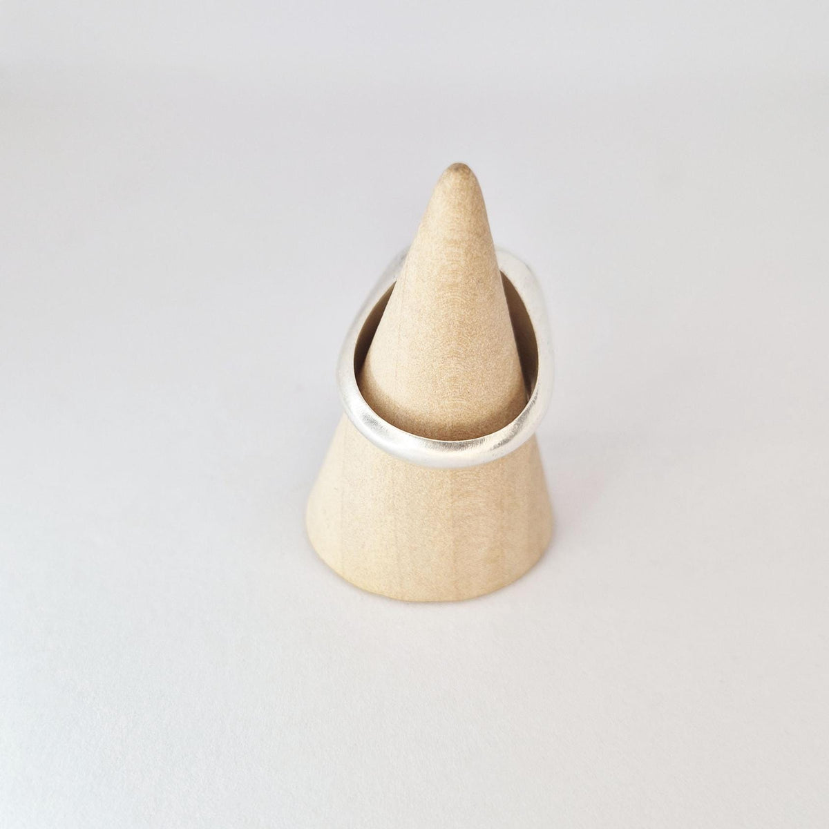 Round signet ring displayed on wooden cone stand, featuring large flat 18mm face with brushed silver finish.