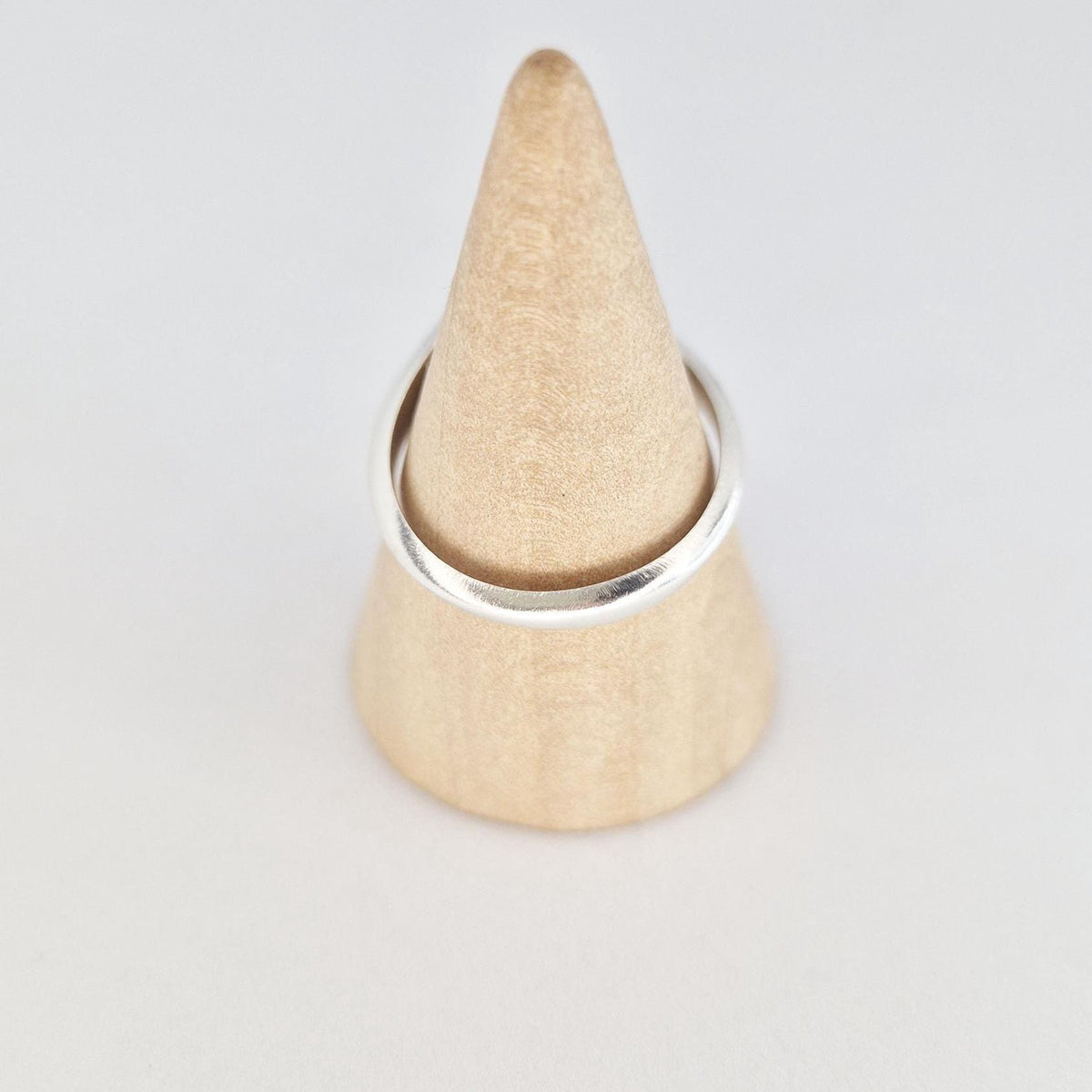 Sterling silver ring displayed on wooden cone, showing band shape and polished finish