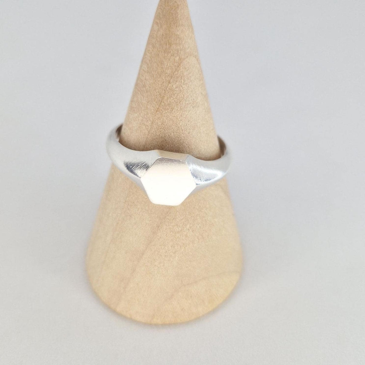 Front view of silver hexagon signet ring on wooden cone, minimalist geometric design