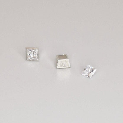 Angled view of square silver bezel setting with gemstone fitted and loose stone beside it