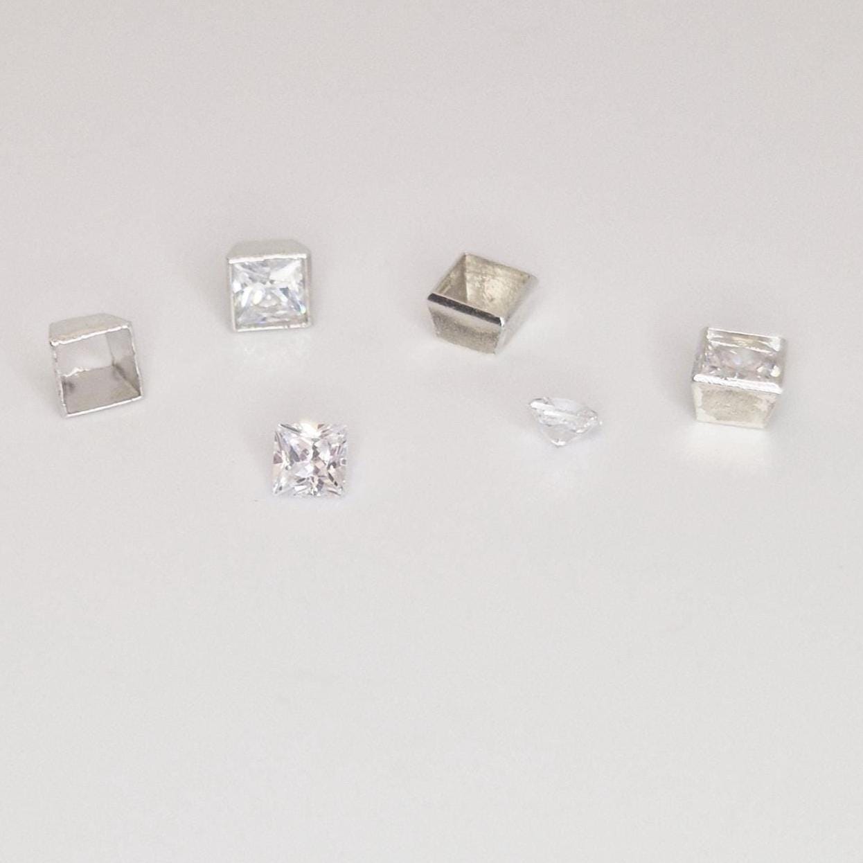 Group of square silver bezel settings and loose princess-cut stones showing scale and variation