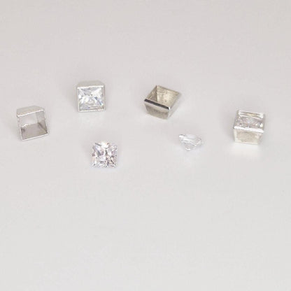 Group of square silver bezel settings and loose princess-cut stones showing scale and variation
