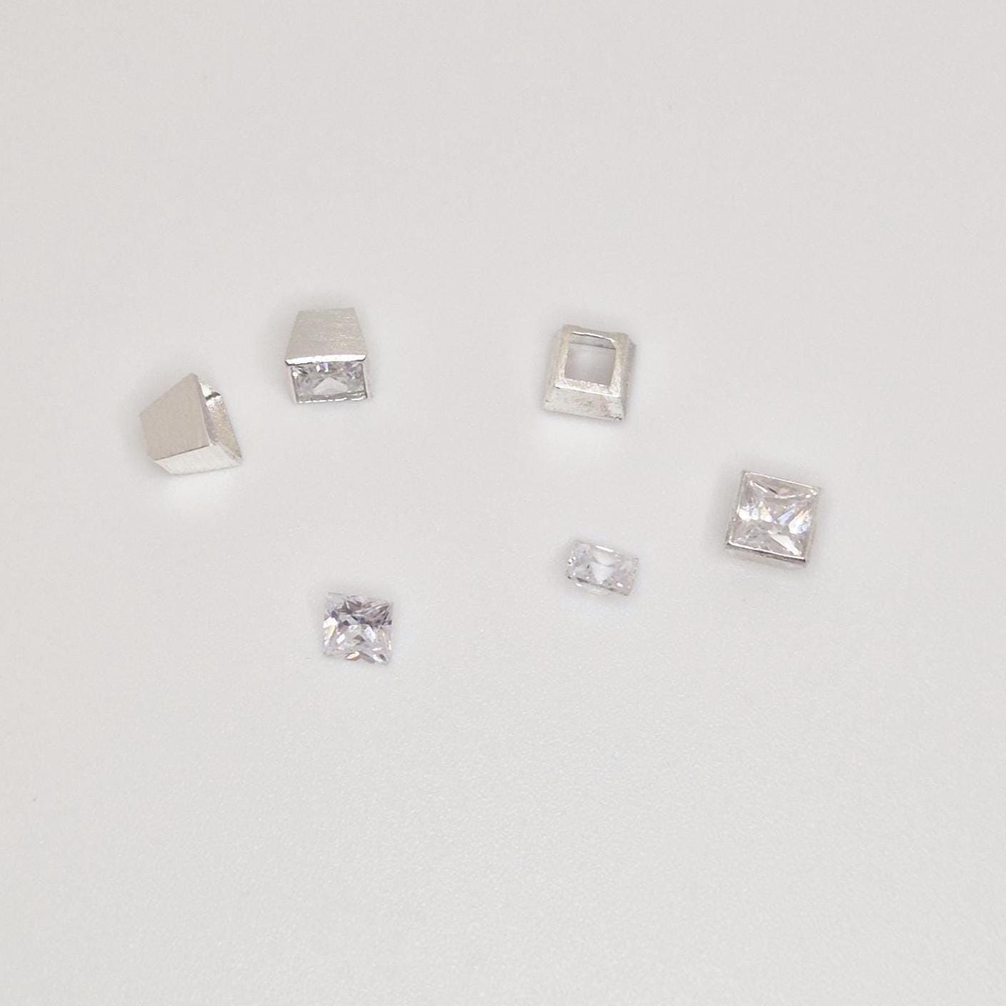 Multiple square bezel settings with princess-cut gemstones arranged on white background