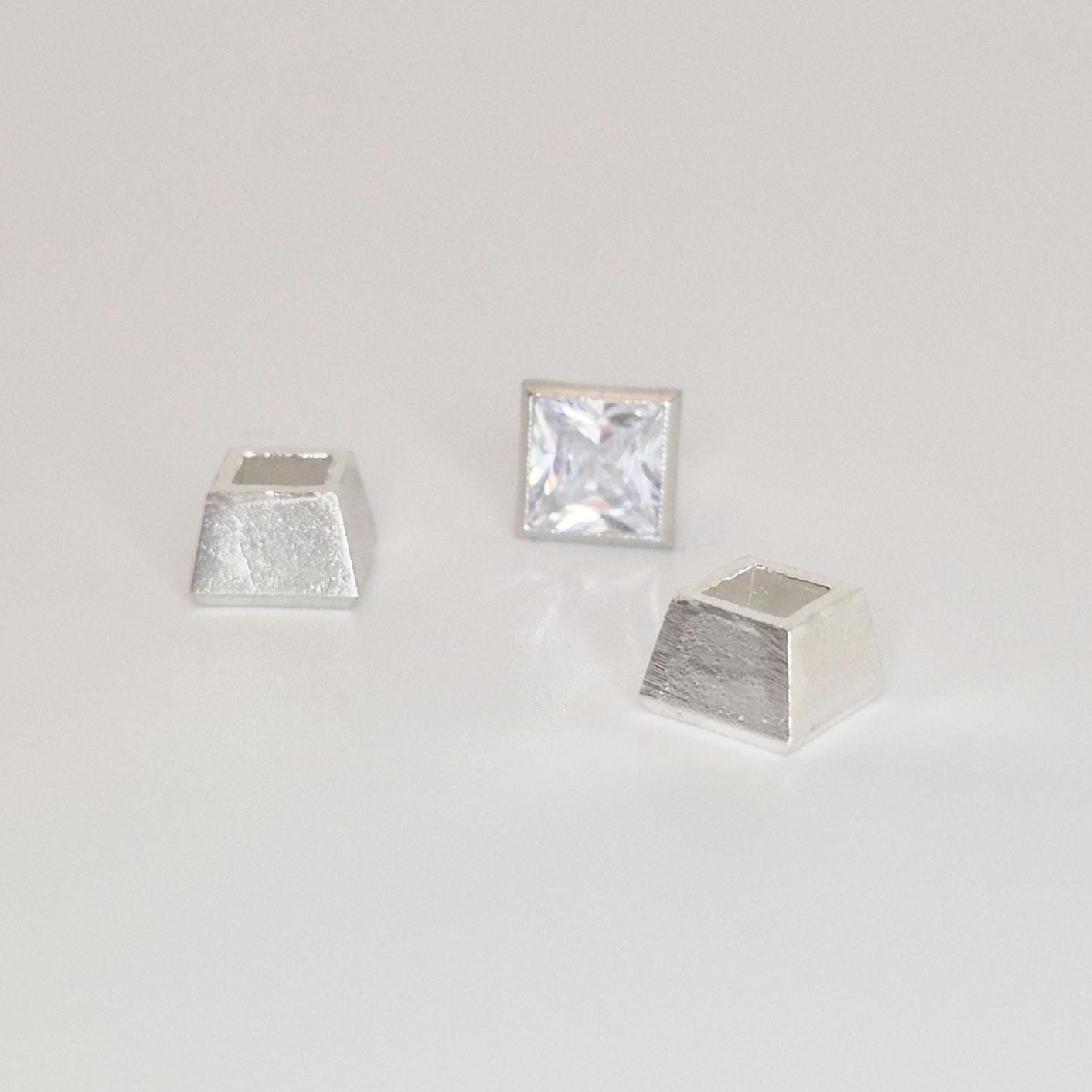 Three-piece sterling silver bezel setting components arranged around a princess cut square gemstone.
