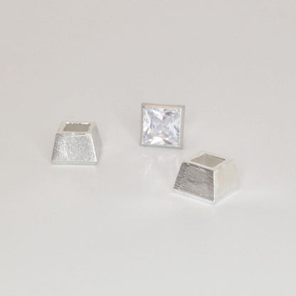 Three-piece sterling silver bezel setting components arranged around a princess cut square gemstone.