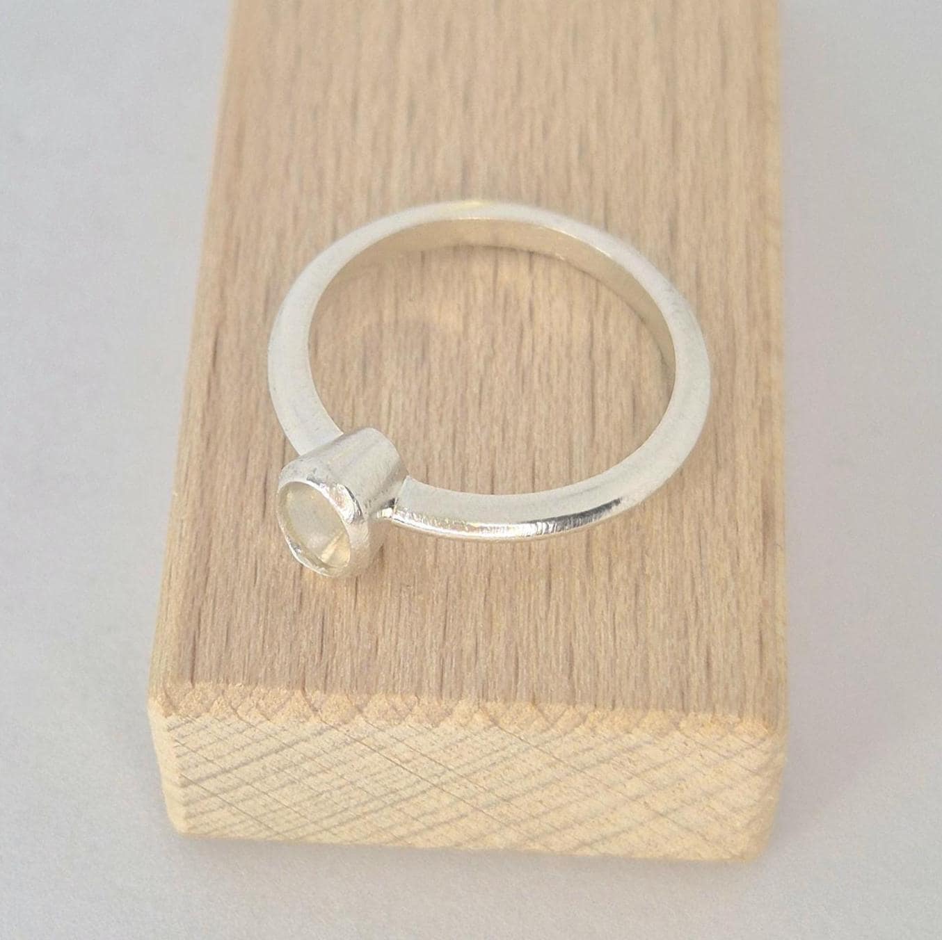 Top view of a sterling silver 6x4mm Oval Bezel Ring on a wooden block against a white background.