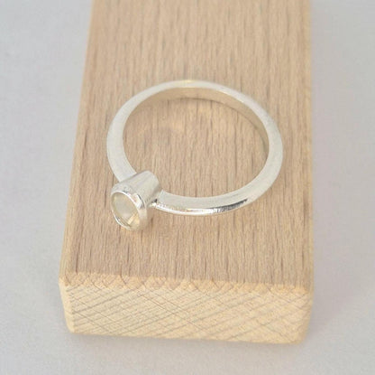 Top view of a sterling silver 6x4mm Oval Bezel Ring on a wooden block against a white background.