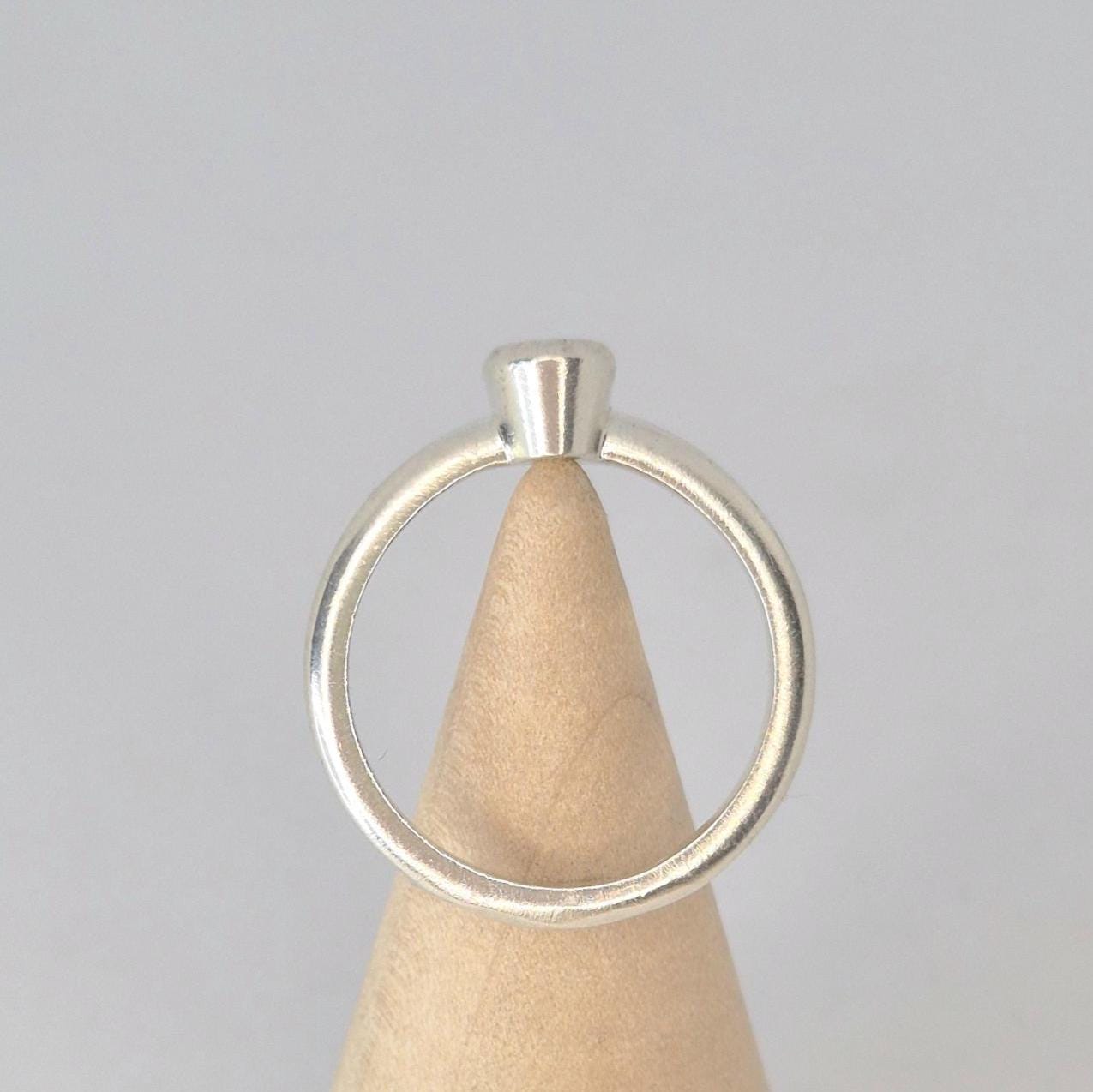 Through finger view of a silver 6x4mm Oval Bezel Ring on the tip of a wooden display cone.