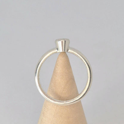 Through finger view of a silver 6x4mm Oval Bezel Ring on the tip of a wooden display cone.