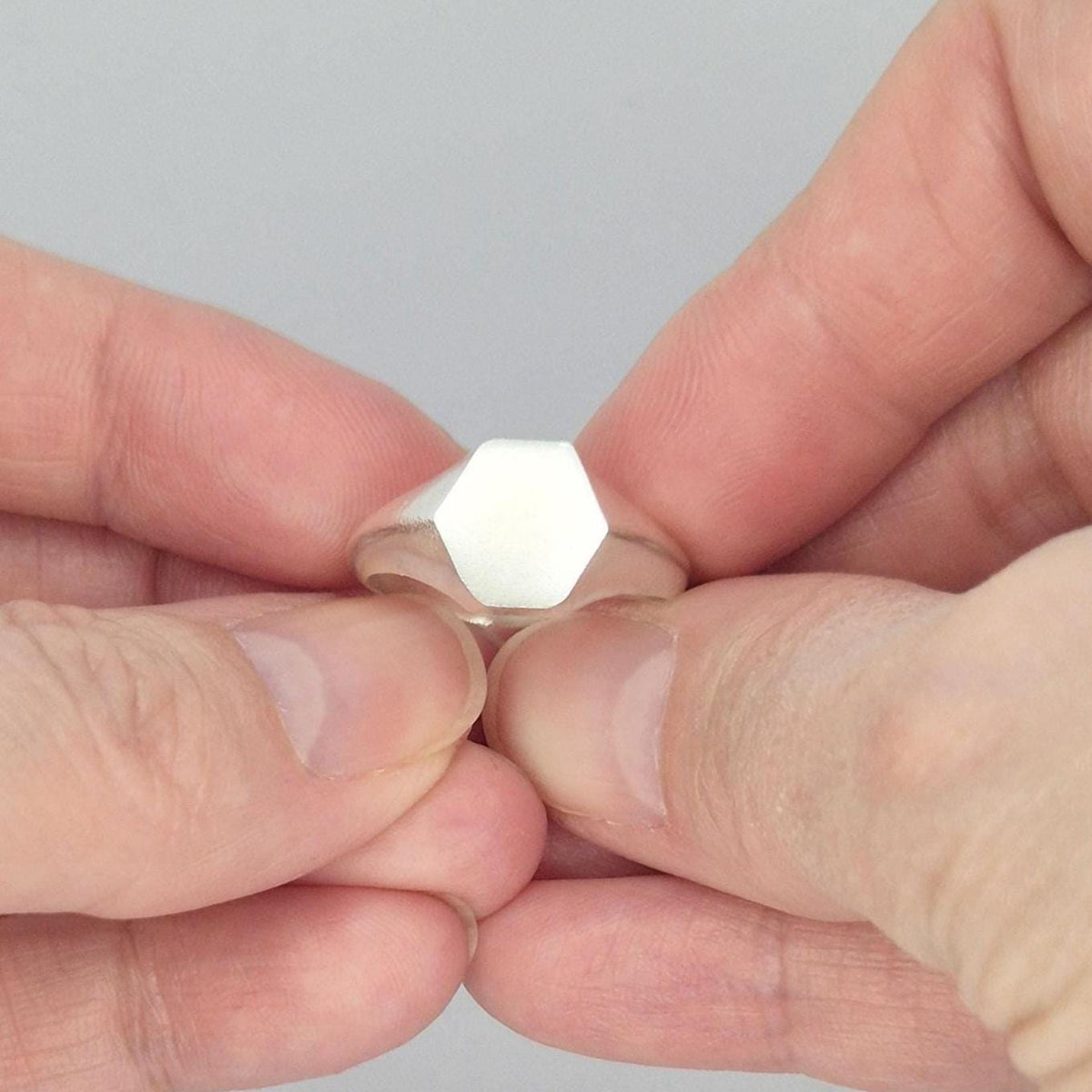 Hexagon signet ring in sterling silver held between fingers, minimalist geometric face with satin finish
