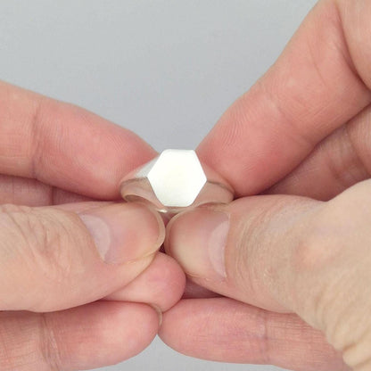 Hexagon signet ring in sterling silver held between fingers, minimalist geometric face with satin finish