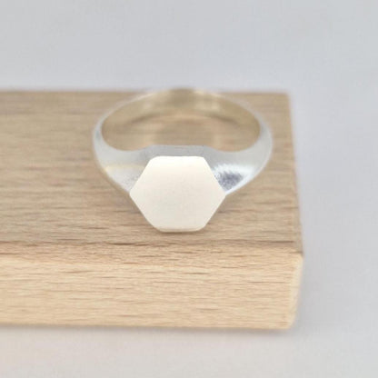 Minimalist hexagon signet ring in silver on wooden block, modern geometric design with polished band
