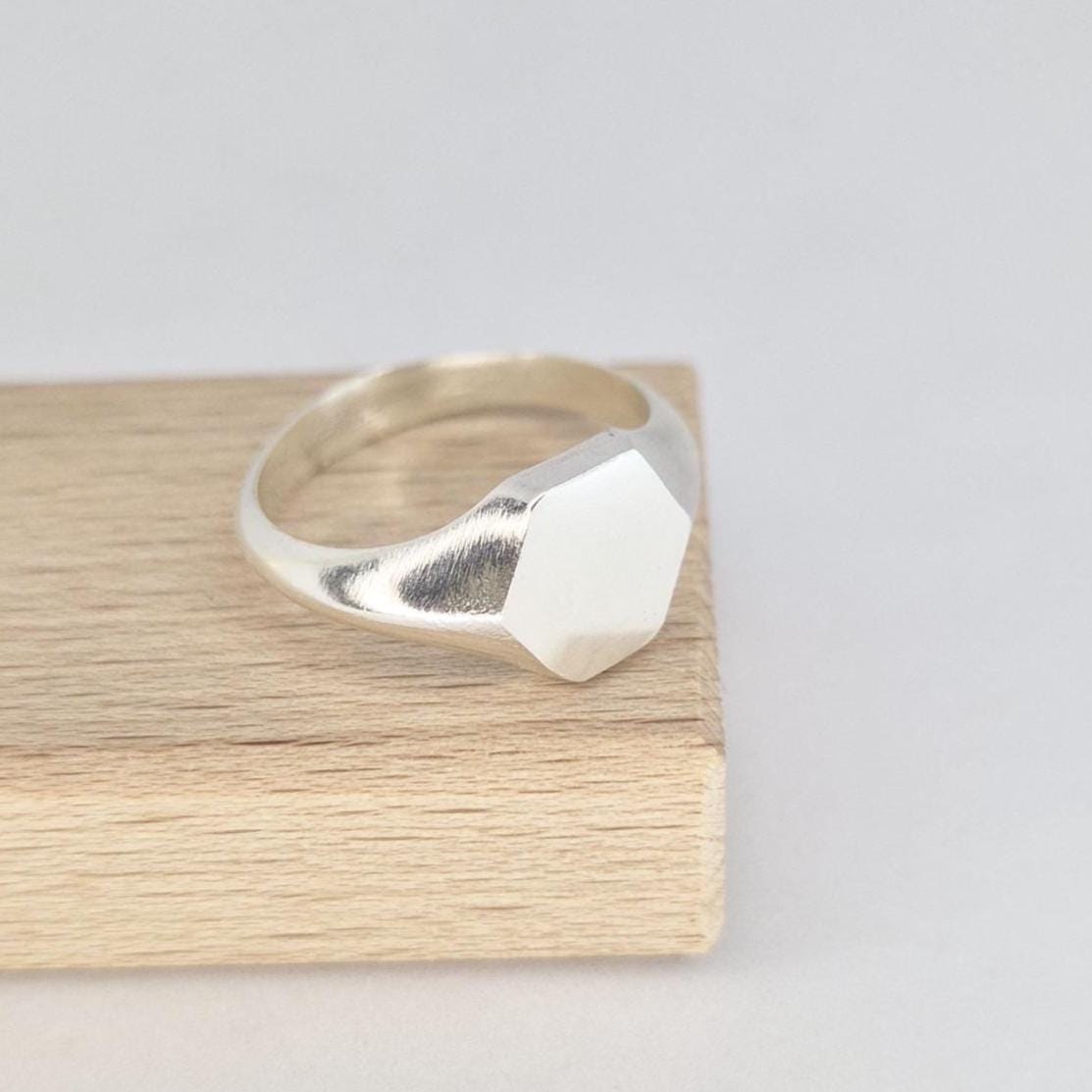 Sterling silver hexagon signet ring side angle on wood, showing tapered shoulders and satin face